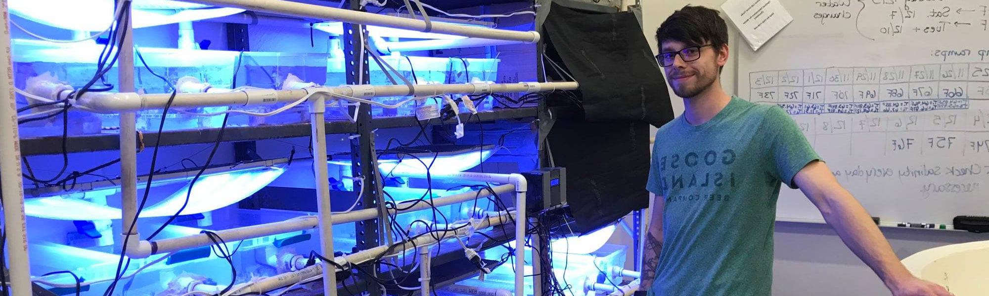 MS Biology Graduate Student Tyler Harman at the Annis Water Resources Institute in Muskegon conducting research on cold-water corals and posing in front of custom recirculating aquarium system.