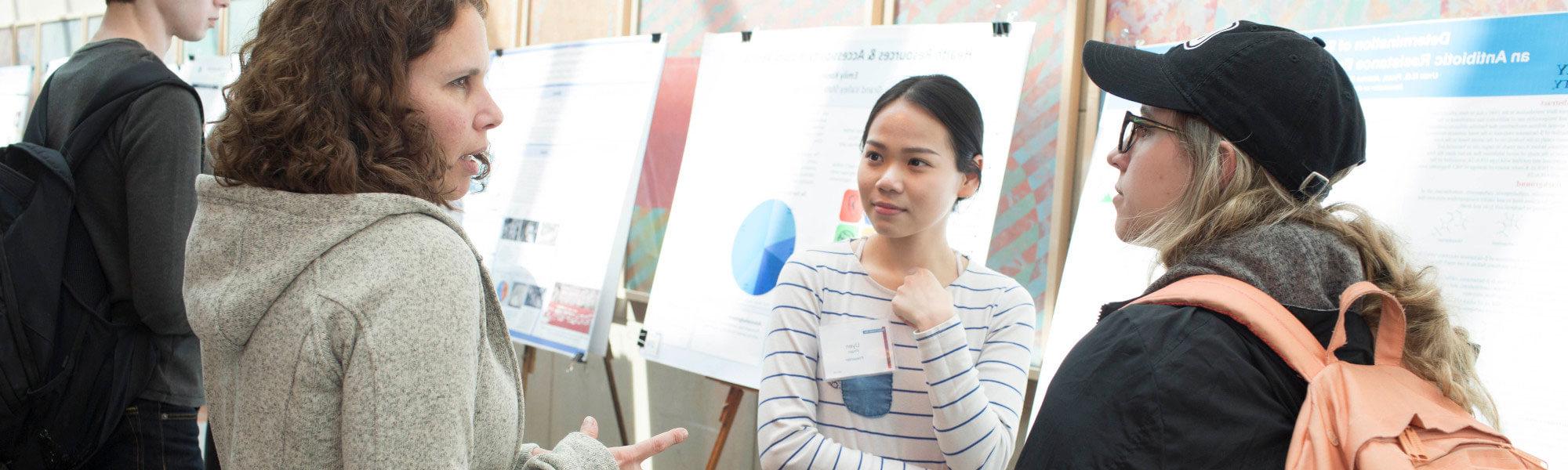 Students discuss a research poster being presented by another student.